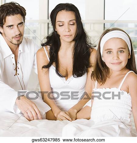 Portrait of a girl sitting on the bed with her parents View Large Photo Image Stock Photography - Portrait of a girl sitting on the bed with her parents. Fotosearch