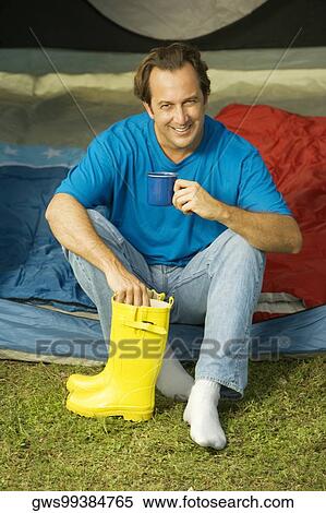 Portrait of a mature man sitting in a tent holding galoshes and a cup View Large Photo Image Stock Photography - Portrait of a mature man sitting in a tent holding galoshes and a cup. Fotosearch