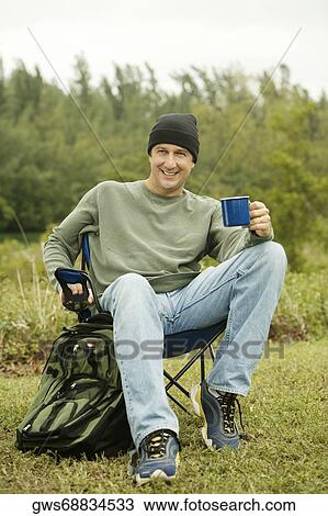 Portrait of a mature man sitting on a folding chair holding a mug View Large Photo Image Stock Image - Portrait of a mature man sitting on a folding chair holding a mug. Fotosearch