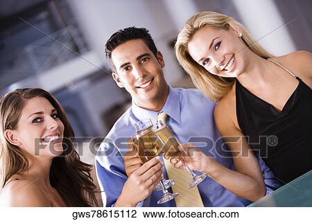 Stock Image - Portrait of a mid adult man and two young women raising a toast. Fotosearch