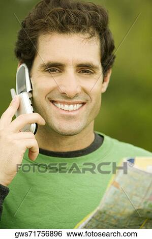 Stock Photograph - Portrait of a mid adult man talking on a mobile phone holding a map. Fotosearch