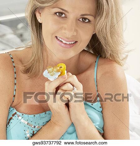 Stock Image - Portrait of a pregnant woman holding two pacifiers. Fotosearch