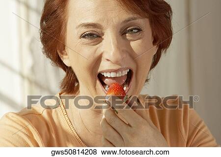 Stock Photo - Portrait of a senior woman eating a strawberry. Fotosearch