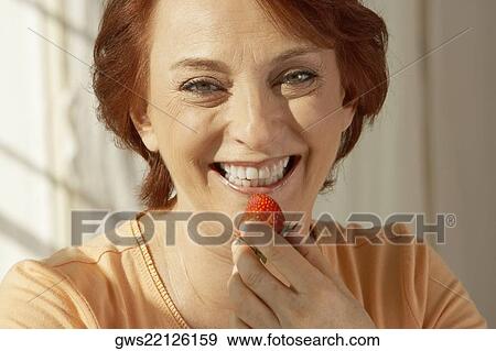 Stock Photo - Portrait of a senior woman holding a strawberry. Fotosearch