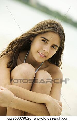 Stock Photograph - Portrait of a teenage girl sitting on the beach smiling. Fotosearch