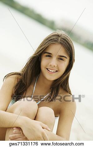 Stock Photograph - Portrait of a teenage girl sitting on the beach smiling. Fotosearch