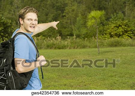 Portrait of a young man carrying a backpack pointing forward View Large Photo Image Stock Photograph - Portrait of a young man carrying a backpack pointing forward. Fotosearch