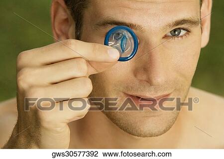 Portrait of a young man holding a condom in front of his eye View Large Photo Image Stock Image - Portrait of a young man holding a condom in front of his eye. Fotosearch
