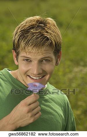 Stock Image - Portrait of a young man holding a flower smiling. Fotosearch