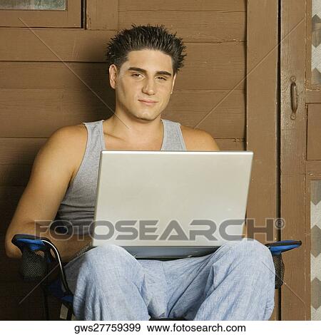 Portrait of a young man sitting on a chair using a laptop View Large Photo Image Stock Photo - Portrait of a young man sitting on a chair using a laptop. Fotosearch