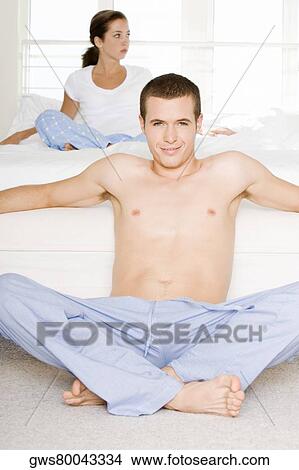 Portrait of a young man sitting on the floor with a young woman sitting behind him on the bed View Large Photo Image Picture - Portrait of a young man sitting on the floor with a young woman sitting behind him on the bed. Fotosearch