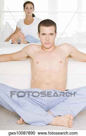 Portrait of a young man sitting on the floor with a young woman sitting behind him on the bed View Large Photo Image Stock Image - Portrait of a young man sitting on the floor with a young woman sitting behind him on the bed. Fotosearch