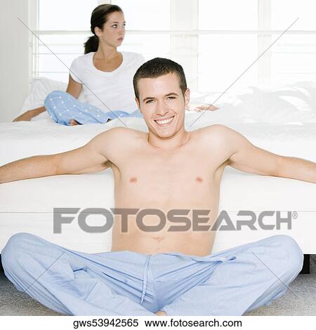 Portrait of a young man sitting on the floor with a young woman sitting behind him on the bed View Large Photo Image Stock Photography - Portrait of a young man sitting on the floor with a young woman sitting behind him on the bed. Fotosearch
