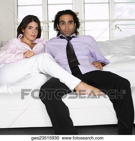 Stock Image - Portrait of a young woman and a mid adult man sitting on the bed. Fotosearch