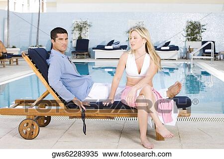 Portrait of a young woman and a mid adult man sitting on a deck chair at the poolside View Large Photo Image Stock Photography - Portrait of a young woman and a mid adult man sitting on a deck chair at the poolside. Fotosearch