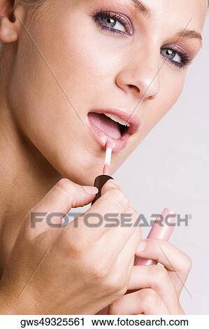 Stock Image - Portrait of a young woman applying lipstick. Fotosearch