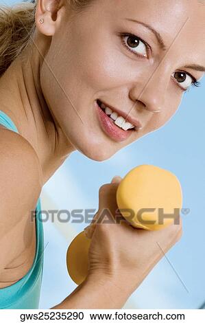 Stock Image - Portrait of a young woman exercising with a dumbbell. Fotosearch