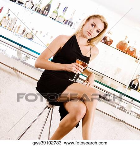 Portrait of a young woman holding a glass of martini in front of a bar counter View Large Photo Image Stock Image - Portrait of a young woman holding a glass of martini in front of a bar counter. Fotosearch