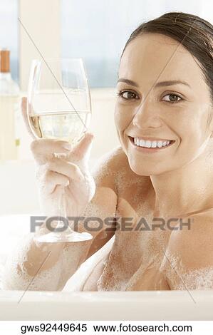 Stock Photography - Portrait of a young woman holding a glass of white wine in the bathtub. Fotosearch