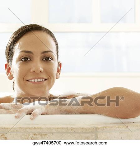 Stock Image - Portrait of a young woman leaning at the edge of a bathtub. Fotosearch