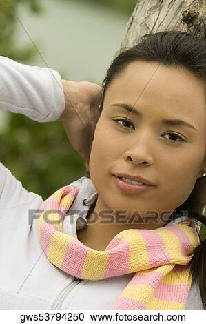 Stock Image - Portrait of a young woman sitting on a tree trunk by the lake. Fotosearch