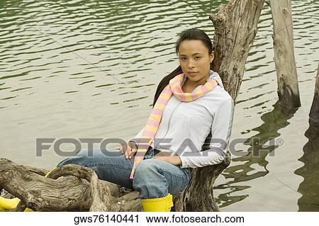 Portrait of a young woman sitting on a tree trunk by the lake View Large Photo Image Stock Image - Portrait of a young woman sitting on a tree trunk by the lake. Fotosearch