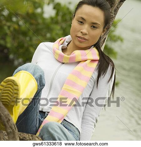 Portrait of a young woman sitting on a tree trunk by the lake View Large Photo Image Stock Photo - Portrait of a young woman sitting on a tree trunk by the lake. Fotosearch