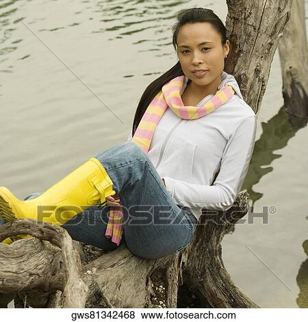Portrait of a young woman sitting on a tree trunk by the lake View Large Photo Image Stock Photo - Portrait of a young woman sitting on a tree trunk by the lake. Fotosearch