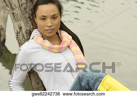 Portrait of a young woman sitting on a tree trunk by the lake View Large Photo Image Stock Photograph - Portrait of a young woman sitting on a tree trunk by the lake. Fotosearch