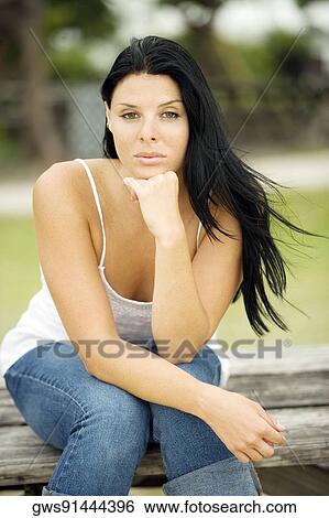Portrait of a young woman sitting on a bench View Large Photo Image Stock Photograph - Portrait of a young woman sitting on a bench. Fotosearch
