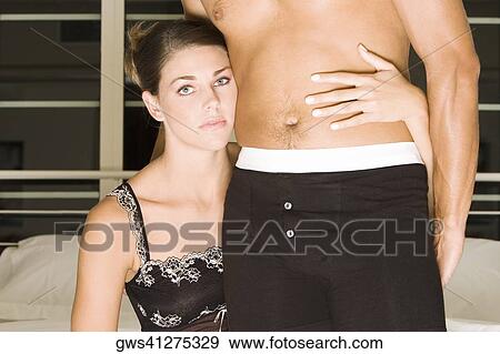 Portrait of a young woman sitting on the bed with her arm around a mid adult man's waist View Large Photo Image Stock Photo - Portrait of a young woman sitting on the bed with her arm around a mid adult man's waist. Fotosearch