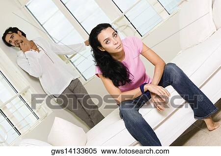 Stock Photography - Portrait of a young woman sitting with a young man leaning against the wall behind her. Fotosearch