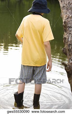 Stock Image - Rear view of a boy standing in water. Fotosearch