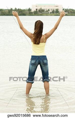Rear view of a girl standing in water with her arms outstretched View Large Photo Image Stock Photograph - Rear view of a girl standing in water with her arms outstretched. Fotosearch