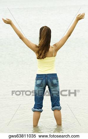 Rear view of a girl standing in water with her arms outstretched View Large Photo Image Stock Photography - Rear view of a girl standing in water with her arms outstretched. Fotosearch