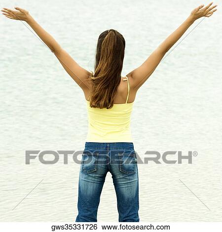 Rear view of a girl standing on the beach with her arms outstretched View Large Photo Image Stock Photograph - Rear view of a girl standing on the beach with her arms outstretched. Fotosearch