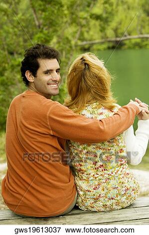 Rear view of a mid adult man sitting with his arm around a young woman View Large Photo Image Stock Photo - Rear view of a mid adult man sitting with his arm around a young woman. Fotosearch