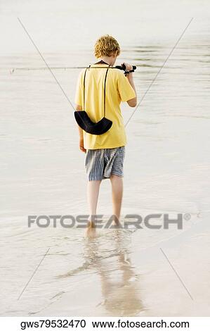 Rear view of a teenage boy walking in a lake with a fishing rod View Large Photo Image Stock Image - Rear view of a teenage boy walking in a lake with a fishing rod. Fotosearch
