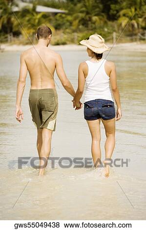 Rear view of a young man and a teenage girl holding hands walking on the beach View Large Photo Image Stock Photo - Rear view of a young man and a teenage girl holding hands walking on the beach. Fotosearch