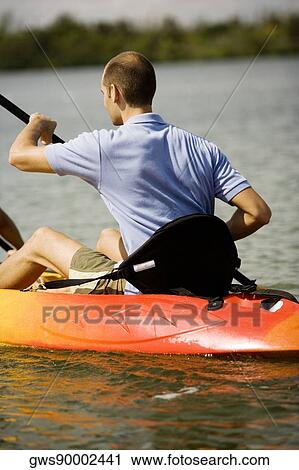 Stock Image - Rear view of a young man kayaking in a lake. Fotosearch