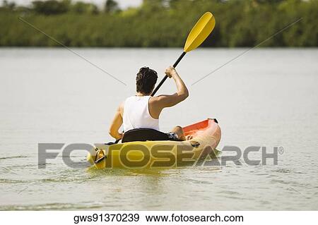 Stock Photo - Rear view of a young man kayaking in a lake. Fotosearch