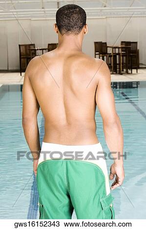 Stock Image - Rear view of a young man standing at the poolside. Fotosearch