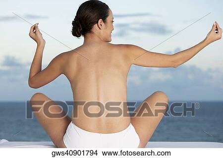 Rear view of a young woman sitting on a massage table with her arms outstretched View Large Photo Image Picture - Rear view of a young woman sitting on a massage table with her arms outstretched. Fotosearch