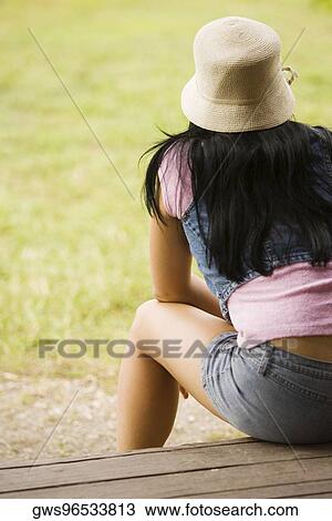 Rear view of a young woman sitting on a bench View Large Photo Image Stock Image - Rear view of a young woman sitting on a bench. Fotosearch