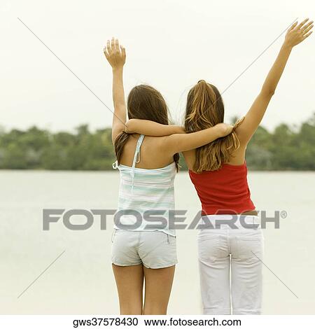 Rear view of girl and a teenage girl standing with their arms around each other on the beach View Large Photo Image Stock Image - Rear view of girl and a teenage girl standing with their arms around each other on the beach. Fotosearch