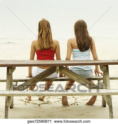 Rear view of girl and a teenage girl sitting on a picnic table on the beach View Large Photo Image Stock Image - Rear view of girl and a teenage girl sitting on a picnic table on the beach. Fotosearch