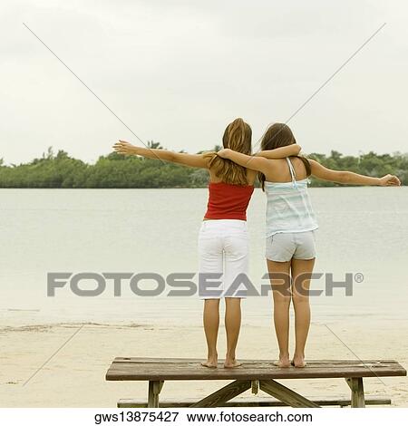 Stock Photo - Rear view of girl and a teenage girl standing with their arms around each other on a picnic table. Fotosearch
