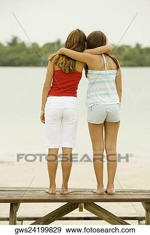 Rear view of girl and a teenage girl standing with their arms around each other on a picnic table View Large Photo Image Stock Photo - Rear view of girl and a teenage girl standing with their arms around each other on a picnic table. Fotosearch