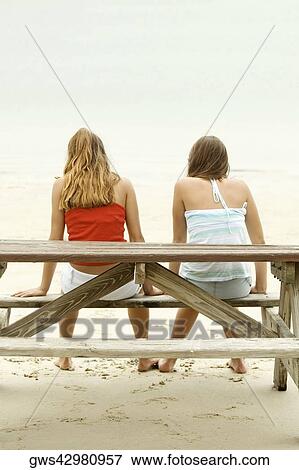 Rear view of girl and a teenage girl sitting on a picnic table on the beach View Large Photo Image Stock Photo - Rear view of girl and a teenage girl sitting on a picnic table on the beach. Fotosearch