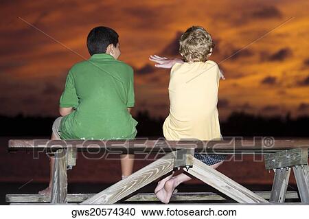 Stock Image - Rear view of two boys sitting on a picnic table. Fotosearch
